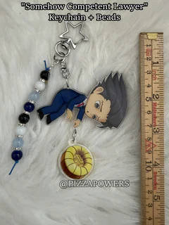 A chibi lawyer with spiky black hair in a blue suit lying on his side, on a star hook with beads and a gold charm